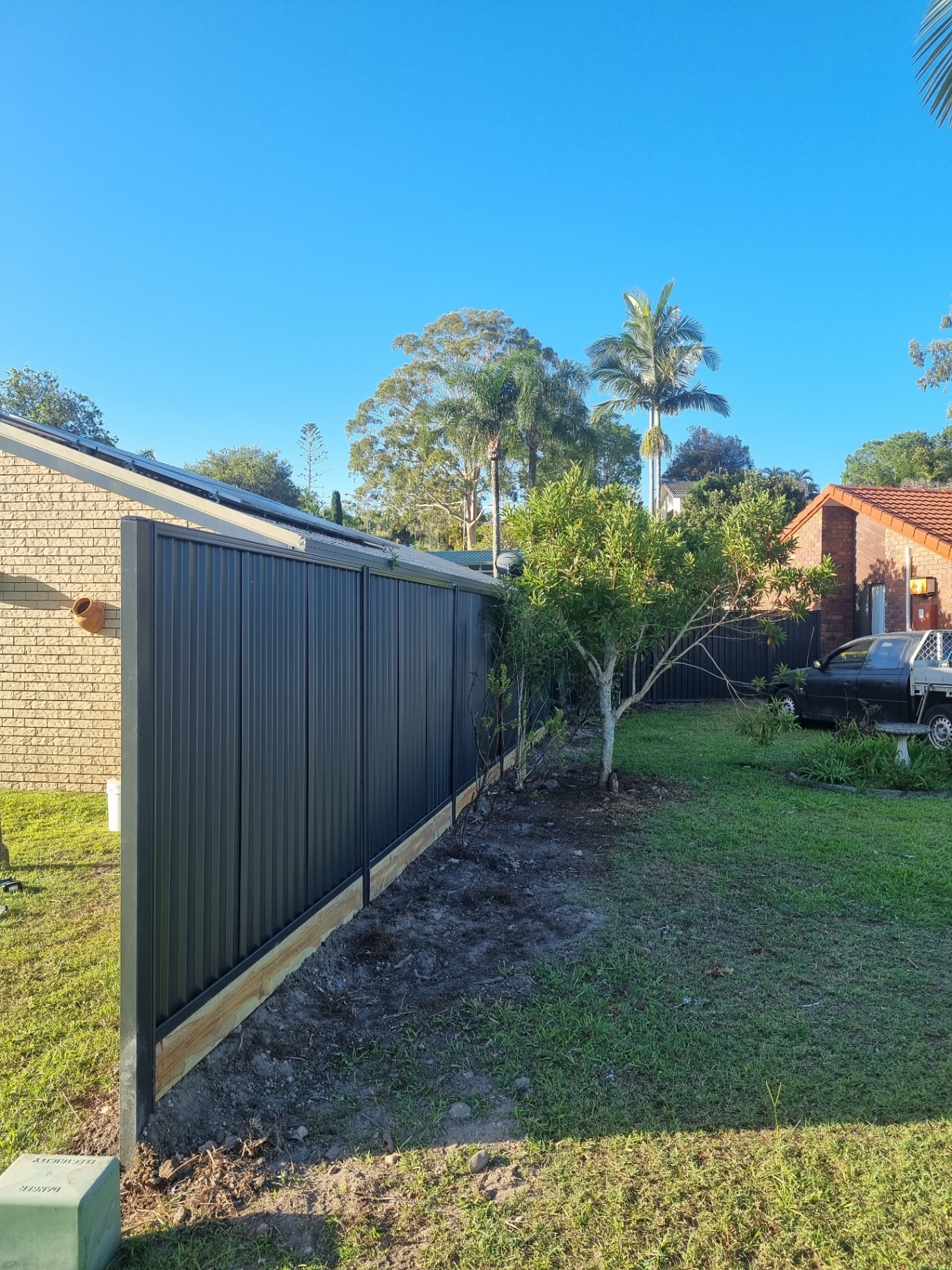 Tall dark Colorbond fence freshly installed with timber plinths along the base.