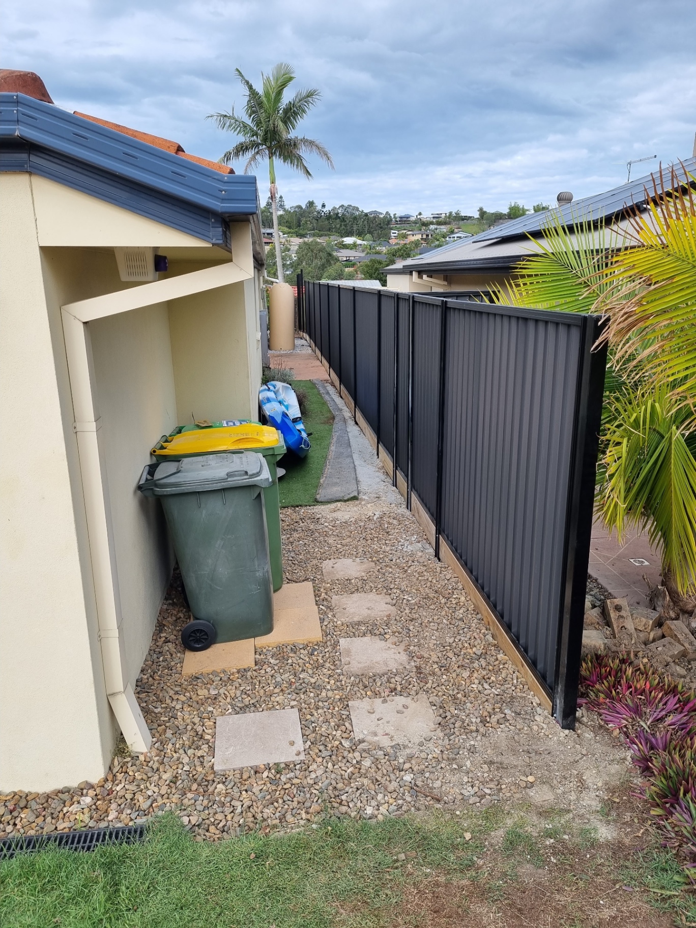 Dark Colorbond fence along a narrow side path with timber sleeper plinths and matching dark posts.
